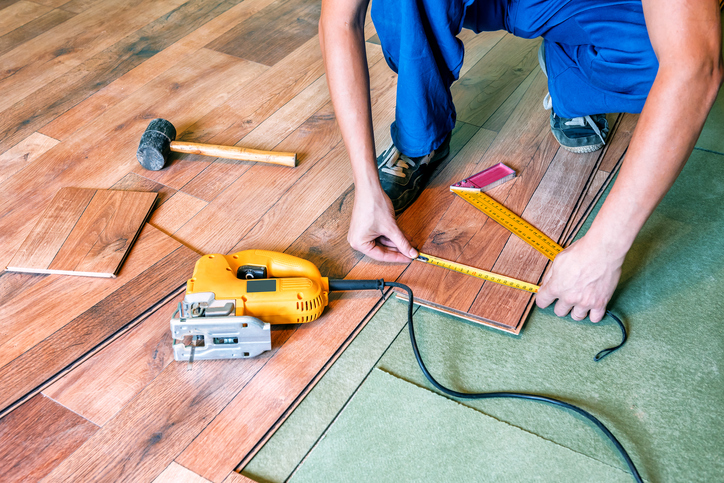 A person using measuring tape and tools while putting in wood paneling on the floor.