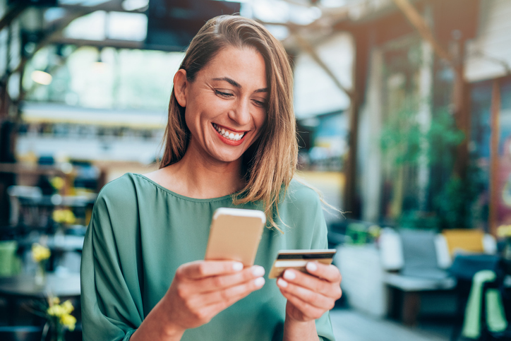 Girl holding credit card and texting A woman using her debit card on her mobile phone.