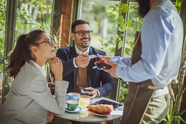 Businessman using a debit card at a restaurant after a business lunch with coworker.